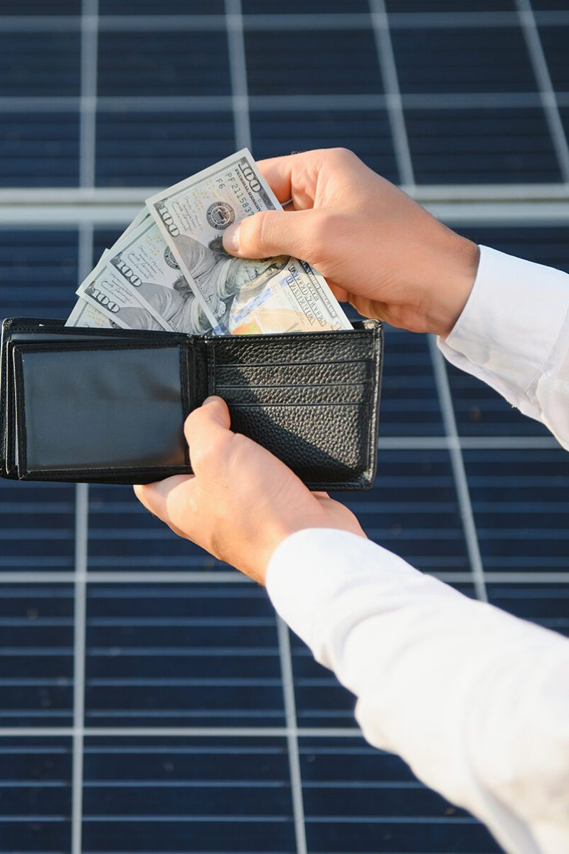 male hand hold hundred dollar at the background of solar station. concept of generation.